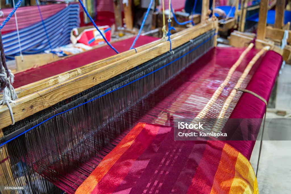 A colorful textile being crafted on a traditional loom, showcasing detailed yarn and precision. Reflecting cultural craftsmanship, the artwork emphasizes skill and heritage in textile creation, blending colors beautifully.